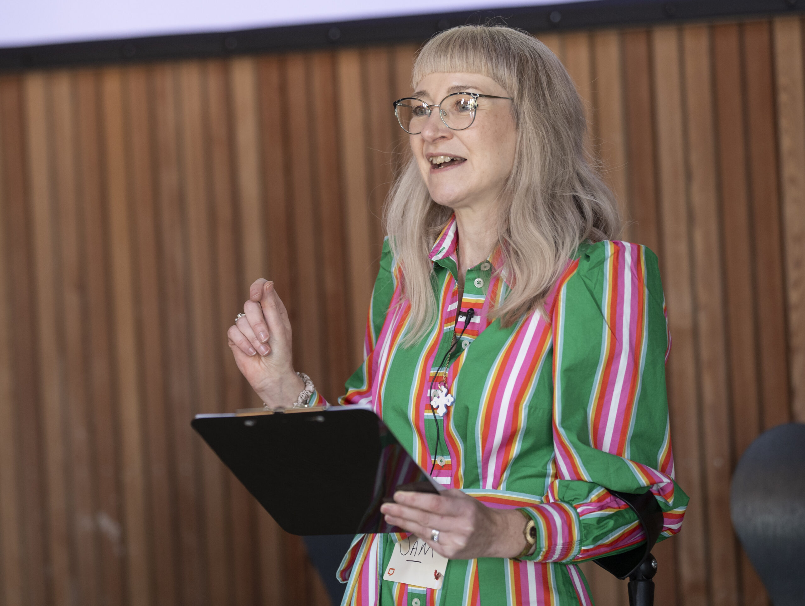 Sam Tonks welcomes participants to The Big Day Out 2024. She's is holding a clipboard with in her left hand. Behind her is a wooden vertical-panelled wall.