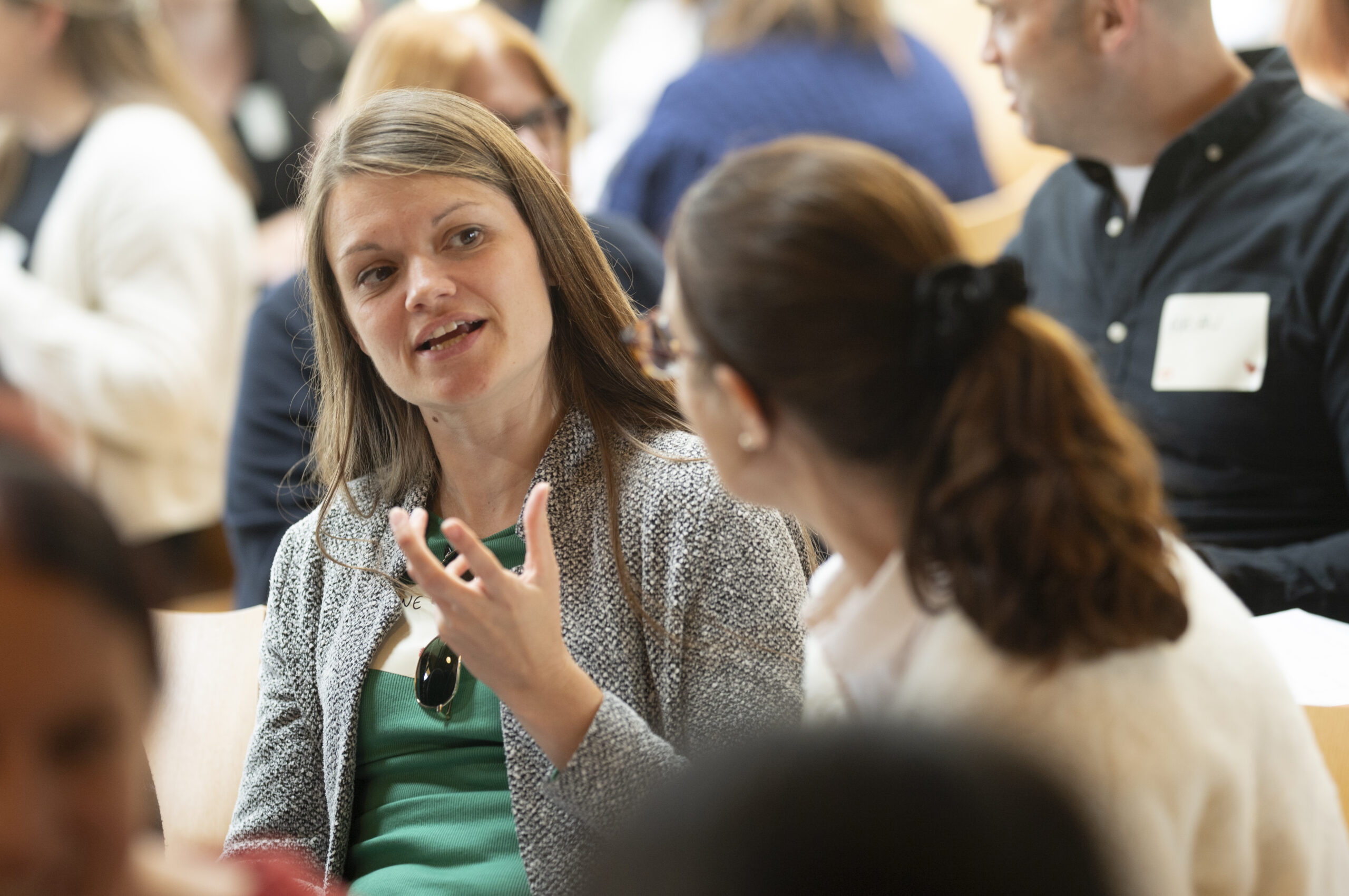 Two people engaged in conversation at what appears to be a professional gathering or networking event. One person is gesturing while speaking animatedly to the other.